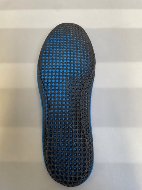 Shoe sole with blue and black perforated mesh pattern on light striped background