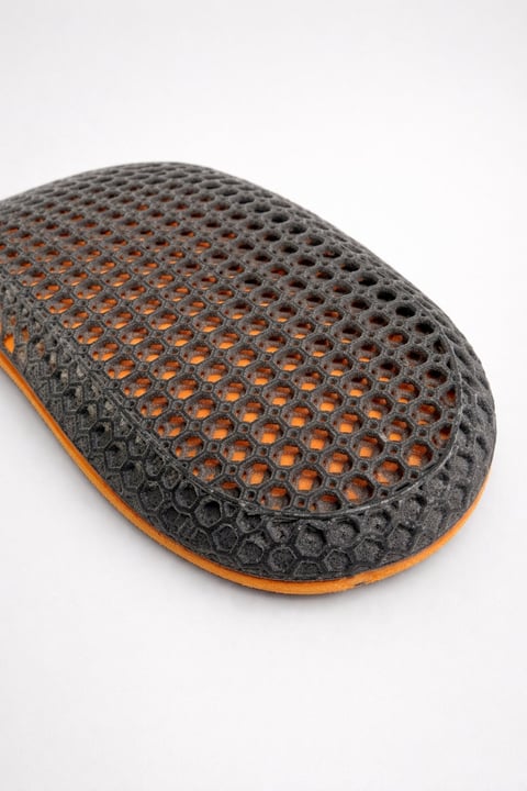 Close-up of a gray perforated shoe sole with orange underlayer and dimpled texture pattern